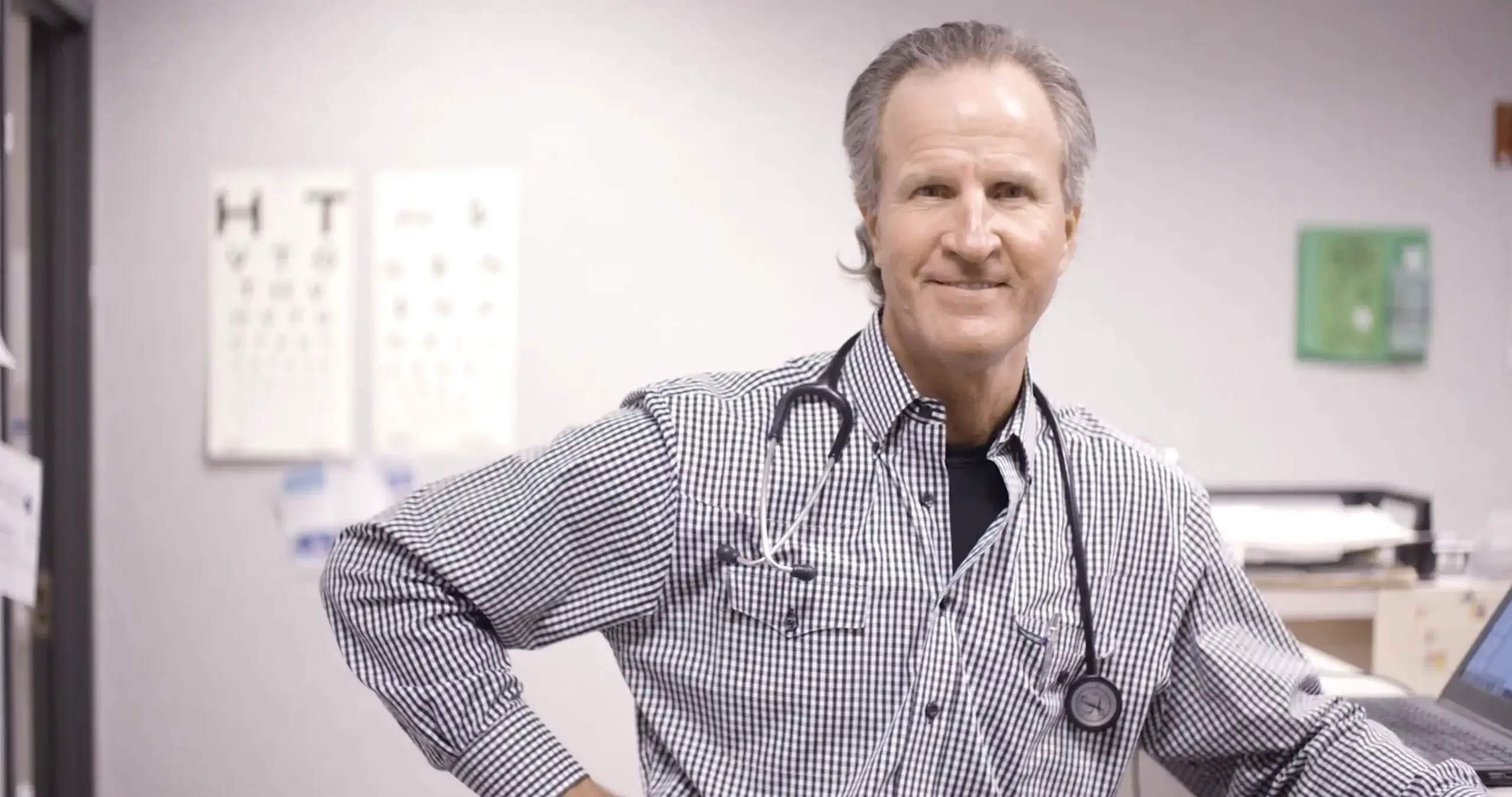 Health care worker wearing a gingham button-down and stethoscope smiles for the crew members of a Dallas healthcare video production company.