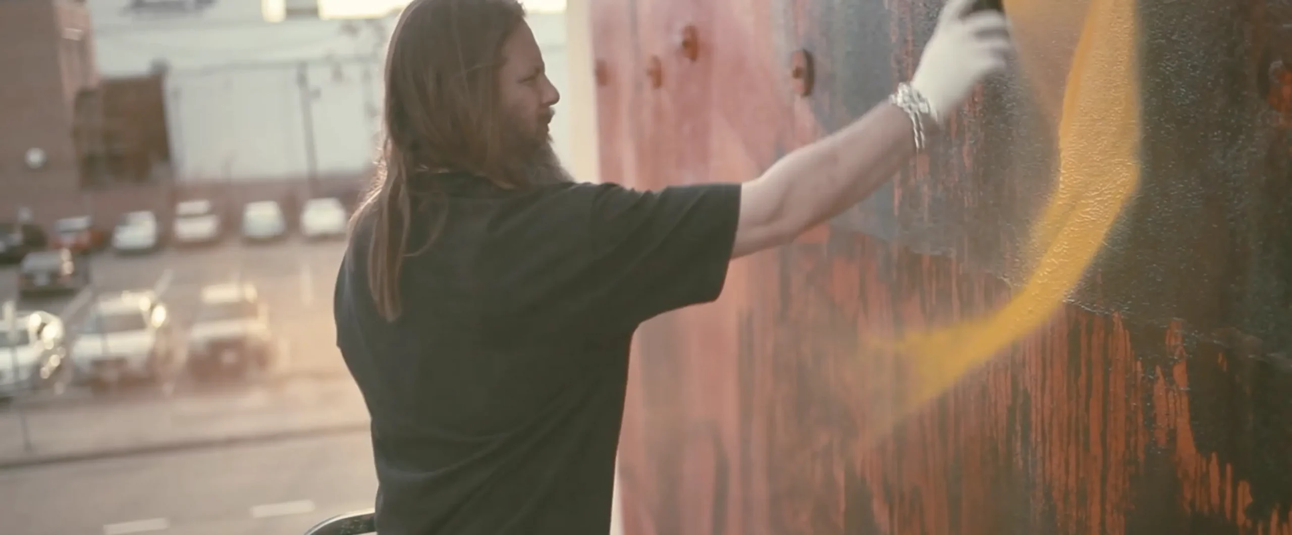 A person wearing gloves and spray painting a wall in Dallas, Texas. The person is being filmed by a branded documentary production company.